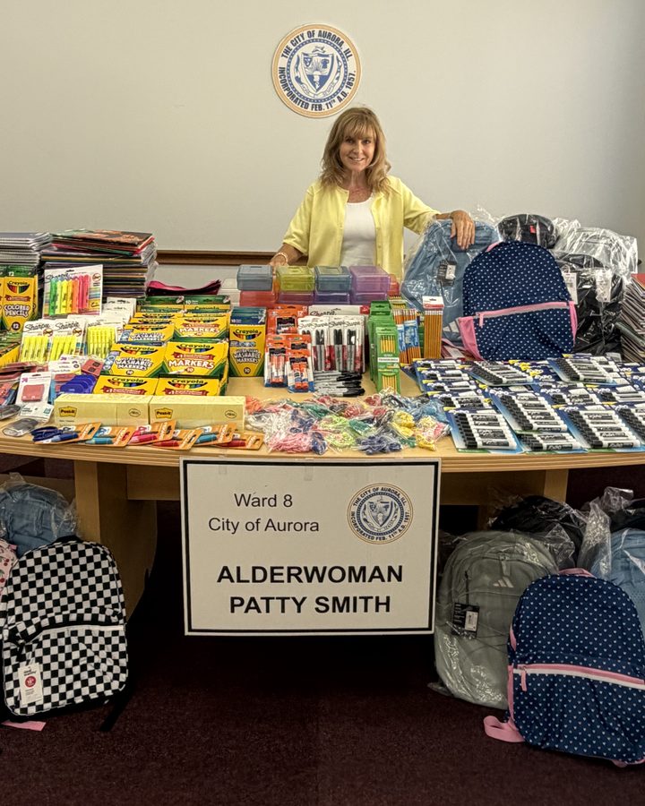 Patty Smith behind a table of donated school supplies, with a sign reading Ward 8, City of Aurora, Alderwoman Patty Smith