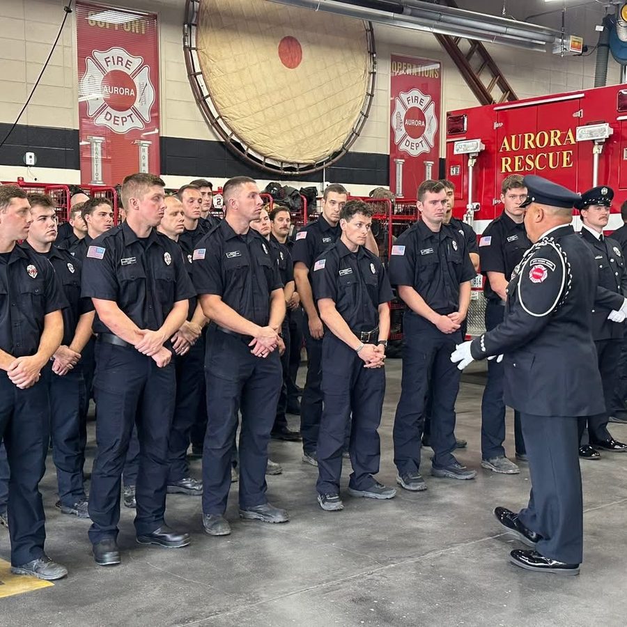 Aurora firefighters lined up in a fire station as an officer in dress uniform speaks to them