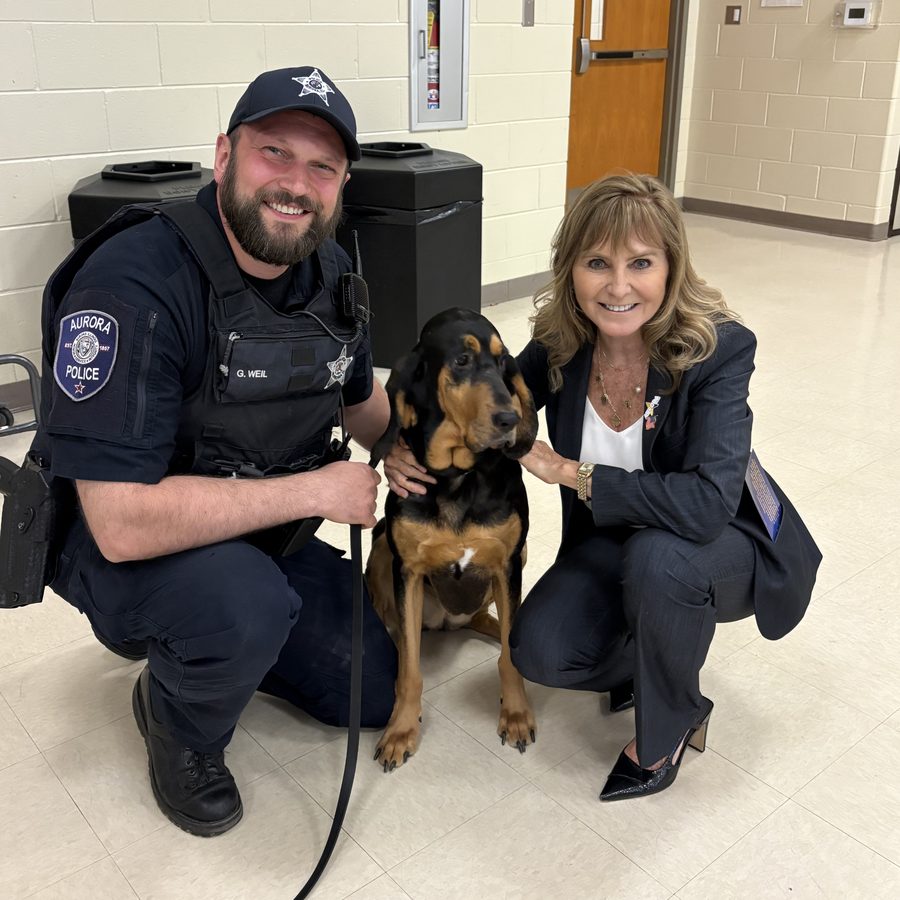 Patty Smith kneeling beside an Aurora police officer and a bloodhound K9
