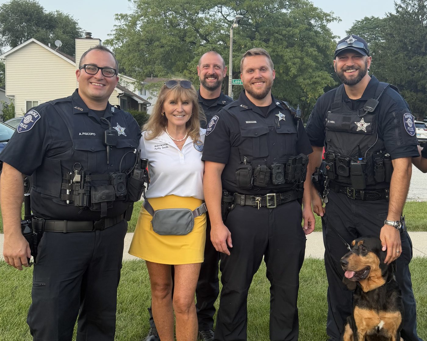 Patty Smith standing on a neighborhood lawn with four Aurora police officers and a police dog