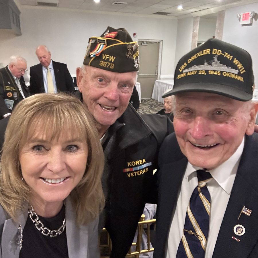 Patty Smith taking a selfie with a Korean War veteran in a VFW cap and a World War II Navy veteran in a USS Drexler cap